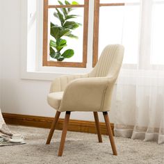 a white chair sitting in front of a window next to a rug and book on the floor