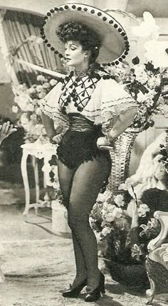 an old photo of a woman wearing a costume and hat with flowers in the background