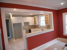 an empty kitchen with red walls and white cabinets in the process of remodeling