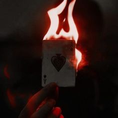 a person holding up a playing card in front of fire