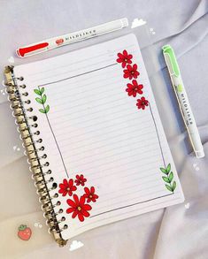 an open notebook with red flowers on it next to a green pen and eraser