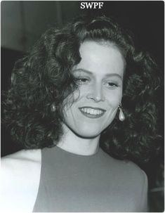 black and white photograph of a woman with curly hair smiling at the camera while wearing earrings