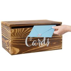 a person holding a blue envelope over a wooden box with the word cards written on it