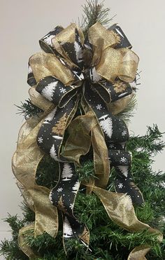 a black and gold christmas tree bow with snowflakes on the top, hanging from a pine tree