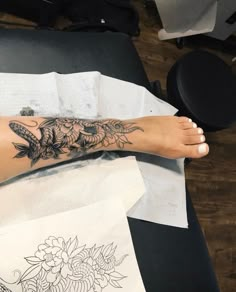 a woman's foot with tattoos on it sitting on top of a table next to papers