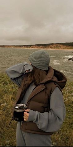 a man standing on top of a lush green field next to the ocean holding a camera