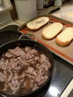 a pan filled with meat sitting on top of a stove next to two bread slices