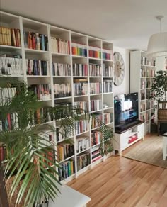 a living room filled with lots of books and furniture next to a tv on top of a wooden floor