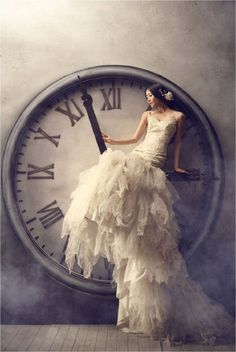 a woman in a white dress standing next to a large clock