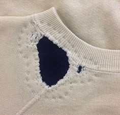 a white sweater with a blue hole in the front and bottom half that has been stitched into it