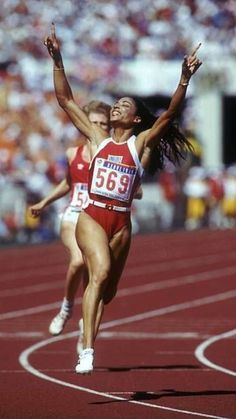 two women running on a track with spectators in the background