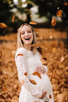 a pregnant woman smiles as she holds her belly in the air surrounded by falling leaves