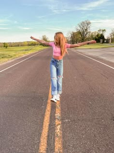 a girl is standing in the middle of an empty road with her arms spread out