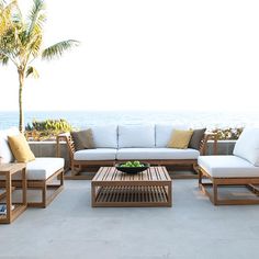 a couch and table sitting on top of a patio next to the ocean with palm trees