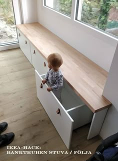 a small child standing in a drawer next to a wooden counter and window sill