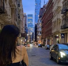 a woman standing in the middle of an empty city street at night with her back to the camera