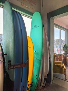 several surfboards are lined up against the wall in front of an open room with large windows