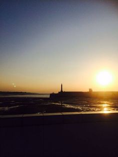 the sun is setting over an ocean with a light house in the distance and water