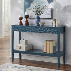 a blue console table with books and vases on it next to a framed painting