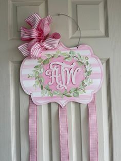 a pink door hanger with a monogrammed wreath and ribbon hanging on it