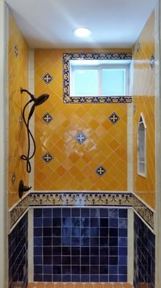 a tiled bathroom with blue and yellow tiles on the walls, shower head, and window