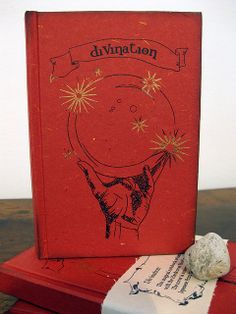 a red book sitting on top of a wooden table next to a rock and paper