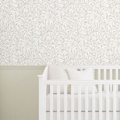 a white crib in front of a wallpapered with leaves