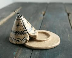 two small clay pots sitting on top of a wooden table next to each other, one with an ornament in the shape of a teepee