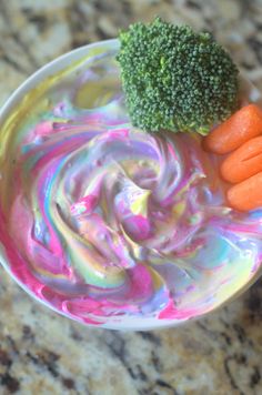 a bowl filled with dip and carrots on top of a marble counter next to broccoli