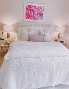 a white bed sitting in a bedroom next to two lamps and a painting on the wall