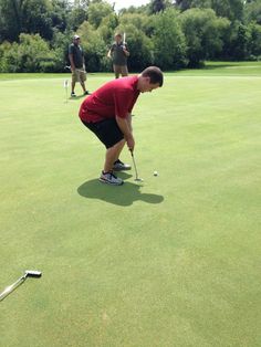 the man is playing golf on the green with two other men in the back ground