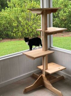 a black cat standing on top of a tall wooden stand in front of a window