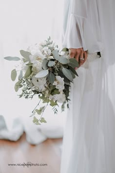 a bride holding a bouquet of white flowers and greenery