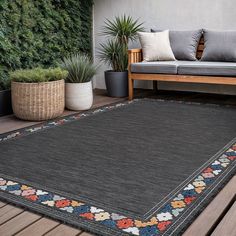 a black rug on a wooden deck with potted plants and couches in the background