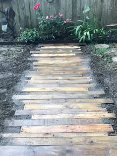 a wooden walkway made out of pallets in front of a fence and flower garden