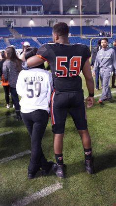 two football players are standing on the field with their arms around each other as they talk