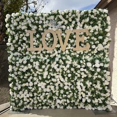 an artificial flower wall with the word love spelled in gold on it's side