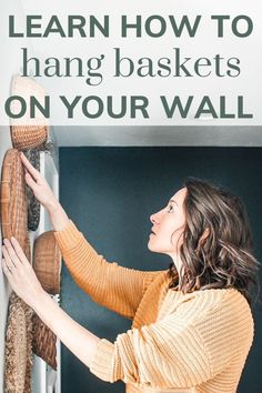 a woman hanging baskets on a wall with the words learn how to hang baskets on your wall