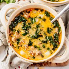 two bowls of soup with meat, spinach and cheese on the side next to a spoon