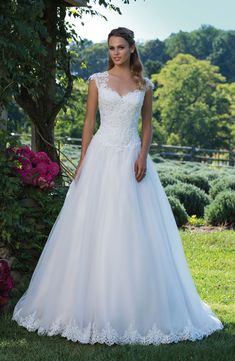 a woman in a white wedding dress standing on the grass near some bushes and flowers