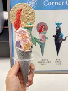 a person holding up an ice cream cone with mermaids on it and other decorations