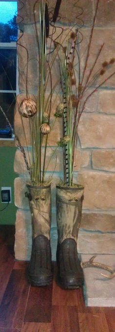 two tall vases with plants in them sitting on a wooden floor next to a brick wall