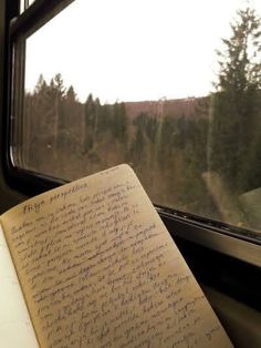 an open book sitting on top of a window sill next to a tree filled forest