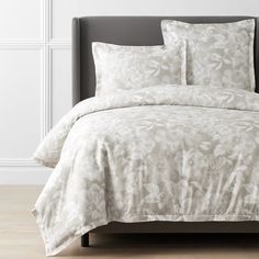 a bed with white comforter and pillows on top of the headboard in front of a wall