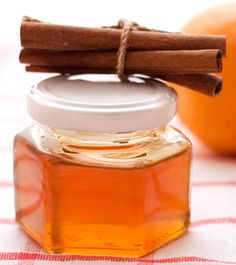 cinnamon sticks sticking out of a jar of honey on a tablecloth with an orange in the background