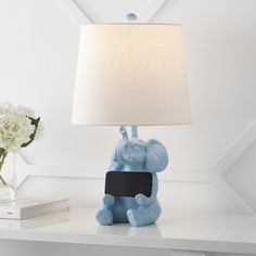 a blue elephant lamp sitting on top of a white table next to a vase with flowers