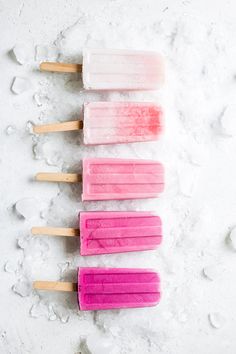 five popsicles are lined up in the snow, one is pink and one is blue