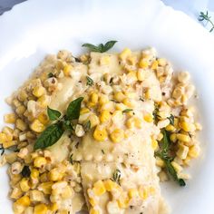 a white plate topped with corn covered in gravy and garnished with green leaves