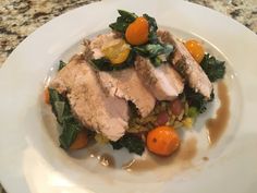 a white plate topped with meat and veggies on top of a marble counter