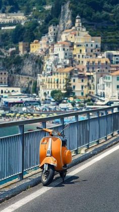 an orange scooter parked on the side of a road next to a body of water